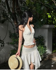 Woman in a white polka dot halter top and mini skirt holding a straw hat outdoors