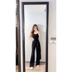 Woman in a black jumpsuit taking a mirror selfie indoors