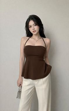 Woman with long dark hair wearing a brown halter top and white pants, holding a silver clutch