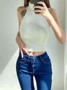 Woman in a white sleeveless turtleneck and blue jeans, exposing her midriff