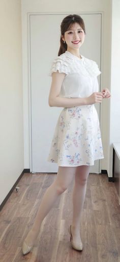 Woman in a white ruffled blouse and floral skirt standing indoors