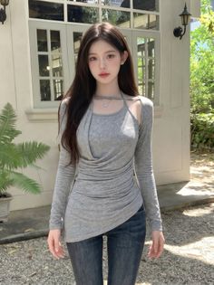 Woman with long dark hair wearing a gray top and jeans outdoors