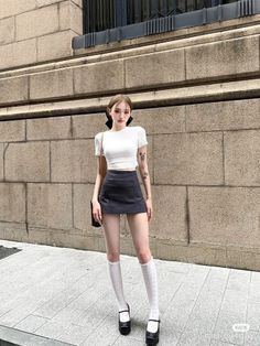 Woman in a white crop top and black mini skirt with knee high socks outdoors