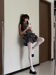 Woman in a plaid dress and white tights taking a mirror selfie
