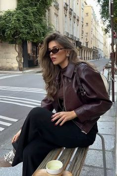 Woman with long hair and sunglasses sitting on a bench on a city street