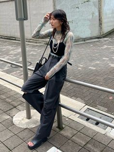 Woman in a sheer top and wide leg pants leaning on a railing outdoors