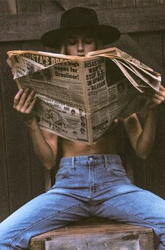 Person in a black hat and blue jeans reading a newspaper, with exposed torso