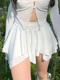 Woman in a white cropped top and skirt outdoors with green grass and purple flowers