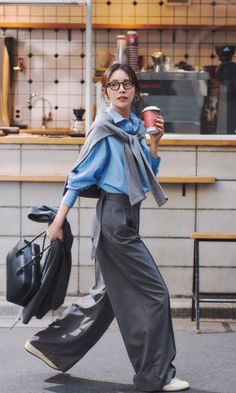 Woman in a blue shirt and wide leg pants walking with a coffee cup