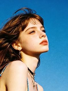 Woman with freckles and long hair looking up against a bright blue sky