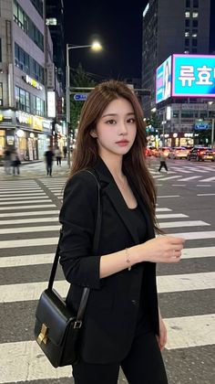 Woman in a black suit standing on a crosswalk in a city at night