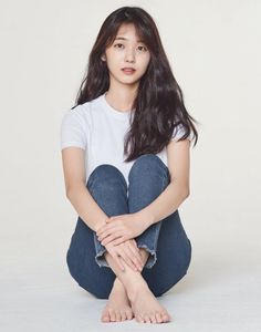 Woman with long dark hair wearing a white t-shirt and blue jeans, sitting on the floor