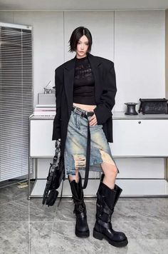 Woman with short black hair wearing a blazer, crop top, ripped denim skirt, and tall boots