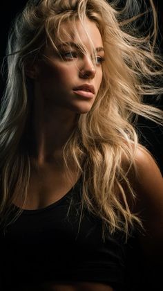 Blonde woman with windblown hair in a black top, dramatically lit