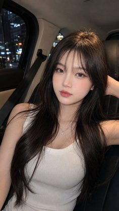 Woman with long dark hair in a white tank top inside a car at night