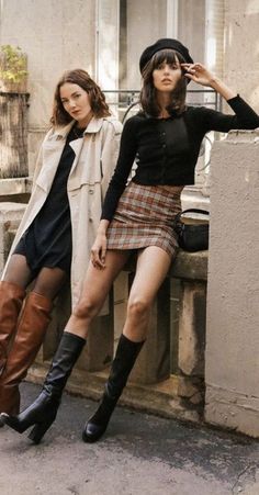 Two women posing outdoors, one in a plaid skirt and beret, the other in a trench coat