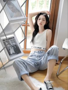 Woman with long black hair wearing a white crop top and loose jeans, sitting indoors
