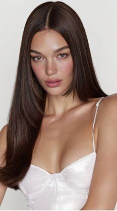 Woman with long brown hair wearing a white top, looking directly at the camera