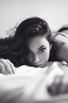 Woman with long hair lying on a bed in a provocative pose, black and white