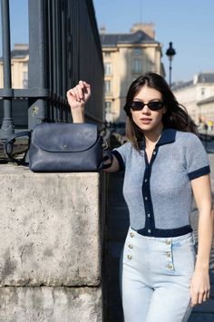 Woman in sunglasses and a blue top with a shoulder bag outdoors