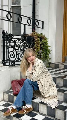Woman with long blonde hair sitting on checkered stairs in a polka dot coat