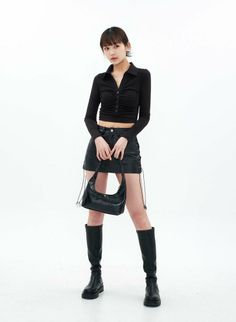 Woman in a black crop top, leather skirt, and knee-high boots holding a handbag