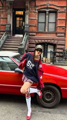 Woman in a plaid skirt and knee-high socks posing next to a red car