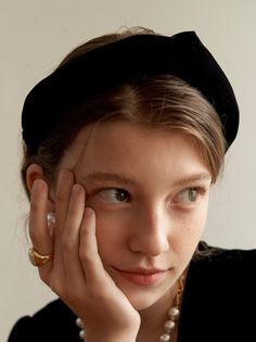 Woman wearing a black headband and pearl necklace, looking to the side