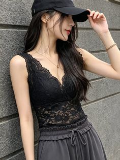 Woman in a black lace top and baseball cap leaning against a wall