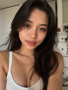 Woman with long dark hair wearing a white tank top and necklace indoors
