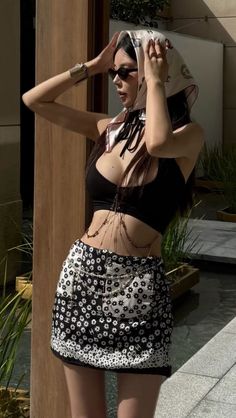Woman in a black crop top and floral mini skirt with a head scarf and sunglasses
