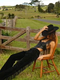 Woman in a cowboy hat and fringe outfit posing on a chair in the countryside