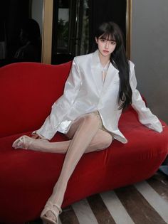 Woman in a white blazer and sheer tights sitting on a red couch