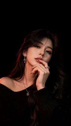 Woman with long dark hair wearing a black sweater and jewelry in dramatic lighting