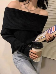 Person in an off-shoulder black sweater holding a book and a coffee cup