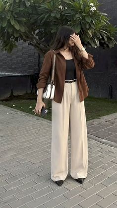 Woman in a brown shirt and wide leg pants holding a phone outdoors