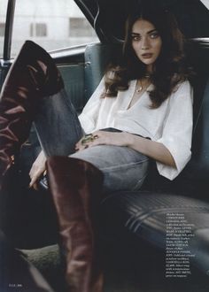 Woman with long dark hair wearing a white shirt and jeans in a car interior