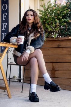 Woman with long wavy hair in a shearling jacket sitting at an outdoor cafe