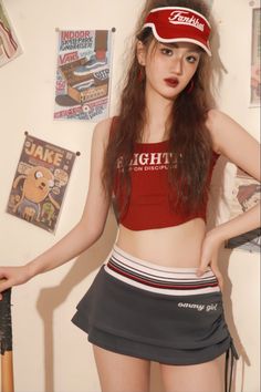 Woman in a red crop top and mini skirt with a red visor indoors