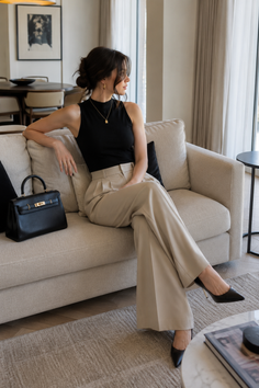 Woman in a black top and wide leg pants sitting on a sofa indoors