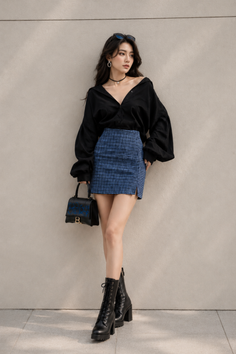 Woman in a black shirt and blue plaid mini skirt with combat boots leaning against a wall