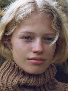 Close up portrait of a young person with blonde hair and blue eyes wearing a turtleneck sweater