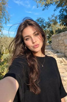 Woman with long brown hair wearing a black shirt outdoors under a blue sky