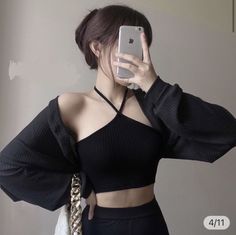 Woman in a black crop top and long sleeve shirt taking a mirror selfie