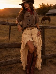 Woman in a cowboy hat and ruffled skirt leaning on a fence at sunset