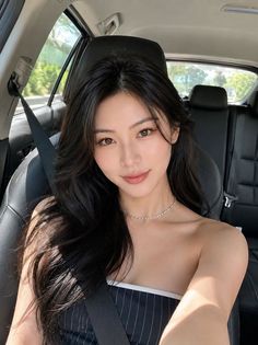 Woman with long black hair wearing a strapless top and necklace in a car