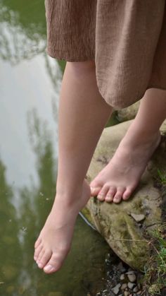 Bare feet of a person in a brown dress touching water from a rock