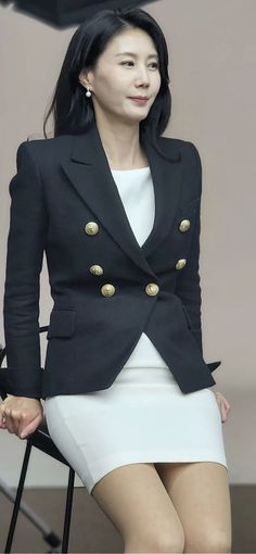Woman in a black blazer and white skirt with long dark hair