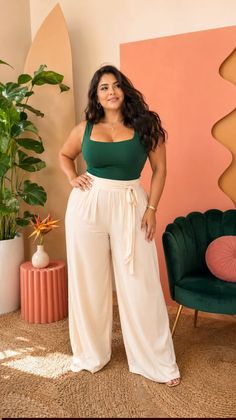 Woman with long dark hair wearing a green top and wide leg pants indoors