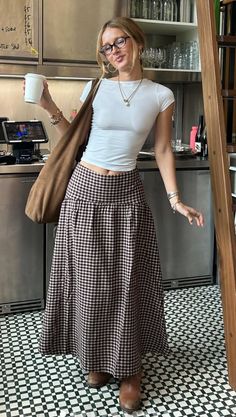 Woman in a white top and plaid skirt holding a cup indoors